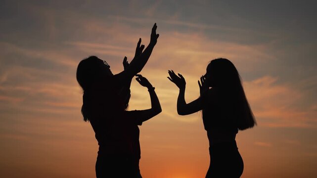 Dancing silhouette group at sunset under orange sky with teen friend trio raising hand to dance conveying joy and celebration outdoor during warm dusk silhouette color amplify dance energy and friend