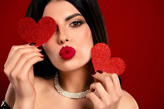 Beautiful young woman with red hearts posing for a Valentine&rsquo;s Day themed photo on red background