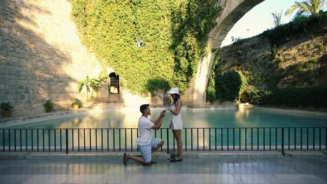 Man kneeling and proposing to woman near pool