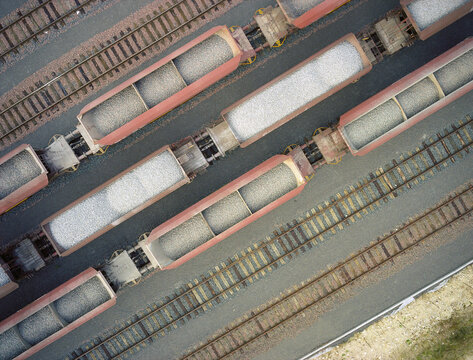 Aerial view of a series of red train cars filled with gravel sit on parallel tracks, contrasting against the grey ground, Reims, Grand Est, France.