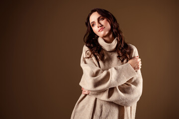 Elegant woman wearing soft beige sweater, posing gracefully with a serene expression, against a warm background