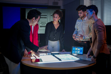 Creative UI/UX design team analyzing mobile app wireframes on illuminated digital touch table. Diverse developers brainstorming web layout strategy in modern high-tech office at night.
