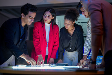 Creative UI/UX design team analyzing mobile app wireframes on illuminated digital touch table. Diverse developers brainstorming web layout strategy in modern high-tech office at night.