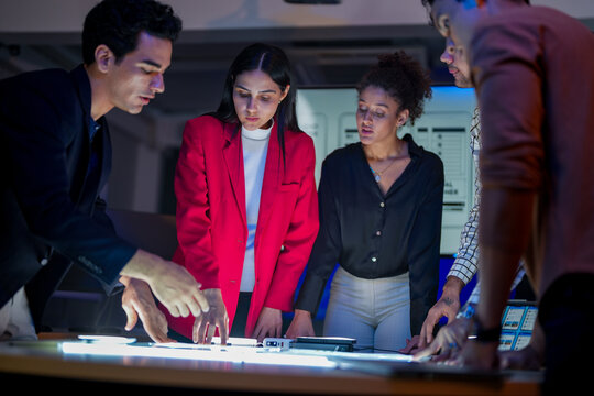 Creative UI/UX design team analyzing mobile app wireframes on illuminated digital touch table. Diverse developers brainstorming web layout strategy in modern high-tech office at night. - Powered by Adobe