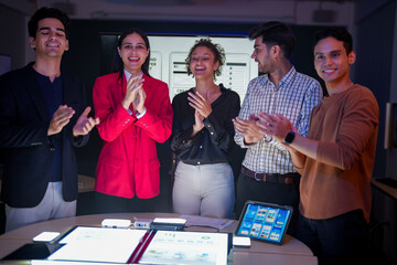 Professional software development team applauding for project success. Happy diverse group clapping hands to celebrate mobile app launch in high-tech startup office.
