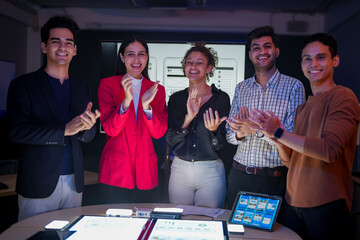 Professional software development team applauding for project success. Happy diverse group clapping hands to celebrate mobile app launch in high-tech startup office.