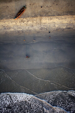 Aerial view of the tranquil beach where the golden sand meets the foamy turquoise waves, with a rustic boat perched nearby, Kozhikode, Kerala, India.
