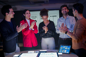 Successful creative team celebrating project achievement in modern office. Happy diverse developers high-fiving after mobile app launch during late night meeting.