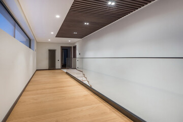 Obraz premium A long bright corridor of a private house. A glass partition separates the stairs. Dark doors at the end of the corridor.