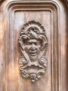 A watchful mascaron in ornate relief adorns a weathered wooden portal.