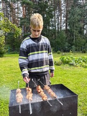 A guy is grilling meat shashlik on a grill on a sunny summer day.