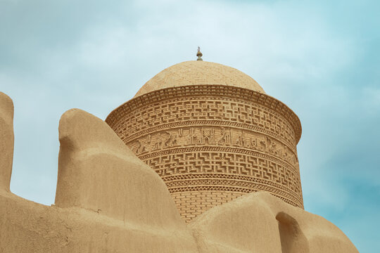 Historical Pir-e Alamdar brick tower with elaborate brick ornaments on a background of cloudy blue sky. The building is located in Damghan City Iran.