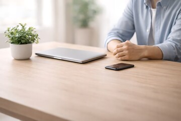 Minimalist office workspace with a closed laptop, smartphone, and small plant on a light wooden table, remote work concept