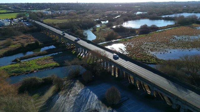Top down aerial view of vehicles cars and traffic crossing archway bridge over the River Nene near Wellingborough, United Kingdom. Winter bright sunlight. Transport and logistics commuting