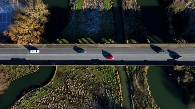Top down aerial view of vehicles cars and traffic crossing archway bridge over the River Nene near Wellingborough, United Kingdom. Winter bright sunlight. Transport and logistics commuting