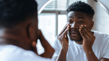 Man stands in front of a mirror, applying skincare product to his face. The room has good lighting...