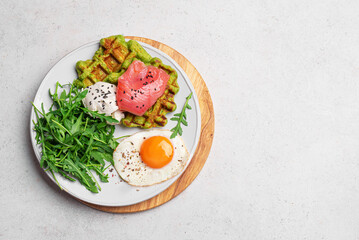 Healthy breakfast with green spinach waffles, salmon, cream cheese, fried egg and salad