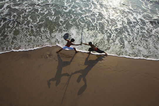 Aerial view of two figures locked in combat on a sandy beach as the surf crashes around them, Kozhikode, Kerala, India.