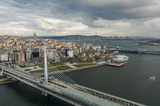 Aerial view of the Halic Metro Bridge stretching across the serene waters of the Golden Horn towards the historic Galata Tower under a brooding sky, Istanbul, Istanbul, Turkey.