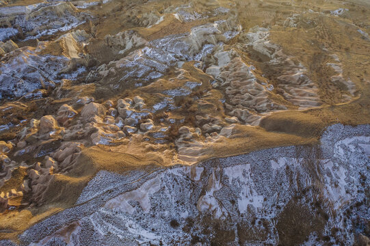 Aerial view of the snow-dusted, sun-kissed fairy chimneys and rock formations create a surreal, otherworldly landscape, Cappadocia, Turkey.