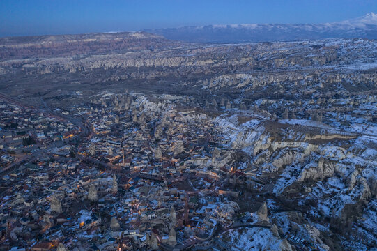 Aerial view of a winter wonderland where snow blankets the surreal landscape of fairy chimneys and ancient dwellings, Cappadocia, Turkey.