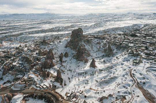 Aerial view of snow-dusted fairy chimneys rise majestically from the stark, wintry landscape, their rugged forms softened by a blanket of white, Cappadocia, Turkey.