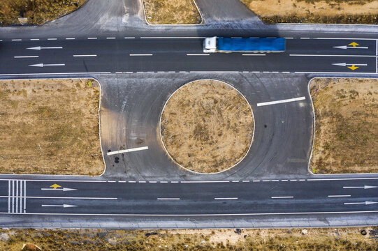 Aerial view of a blue trailer truck navigating a roundabout, the asphalt contrasting with the dry, beige landscape, saray/van, Turkey.