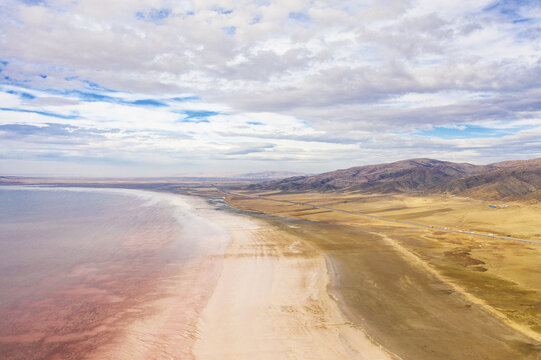 Aerial view of a pink-tinted lake meeting the stark, arid landscape under a vast sky, Lake Tuz, saray/van, Turkey.
