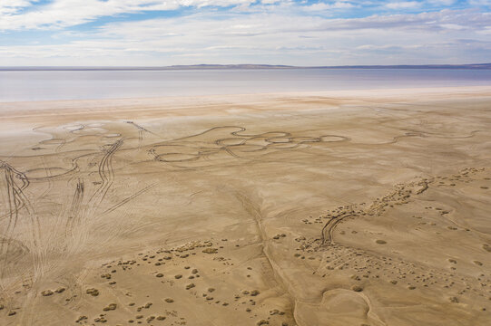 Aerial view of the stark, beige landscape meeting the soft pink hues of the distant lake under a bright, partly cloudy sky, Lake Tuz, saray/van, Turkey.