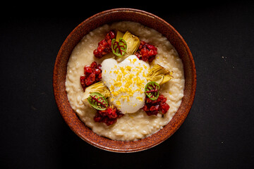 A beautifully crafted risotto bowl features creamy rice, artichokes, red sauce, and a poached egg
