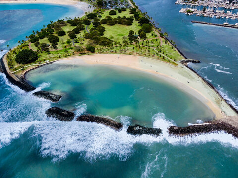 Aerial view of a tranquil lagoon embraced by a crescent of white sand, verdant trees, and rugged breakwaters, Honolulu, Hawaii, United States.