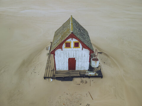 Aerial view of a solitary house with red accents stands out against the vast expanse of sand, its weathered facade telling tales of coastal life, Costa da Caparica, Setubal, Portugal.