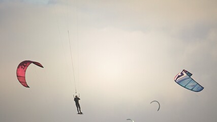 Aerial view of kitesurfers silhouetted against the sky as they ride the wind and waves, a dance of color and motion against the pale canvas, Cape Town, Western Cape, South Africa.