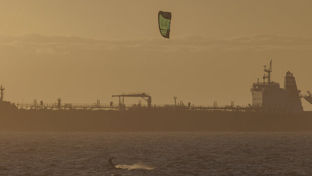 Aerial view of a lone kite surfer dances on the waves beneath a setting sun, dwarfed by a distant tanker, a scene of serene contrast., Cape Town, Western Cape, South Africa.