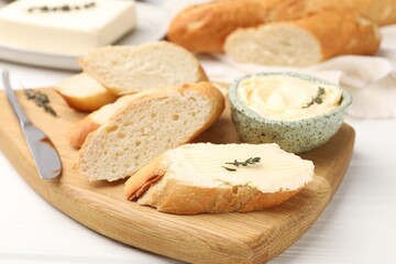 Naklejka premium Slices of baguette with butter, thyme and knife on white wooden table, closeup