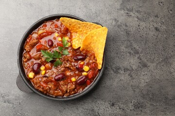 Delicious chili con carne with nachos on grey table, top view. Space for text