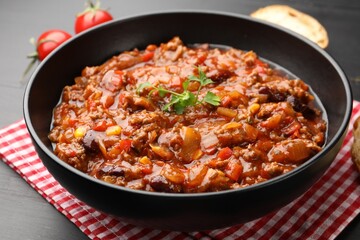 Delicious chili con carne served on black wooden table, closeup