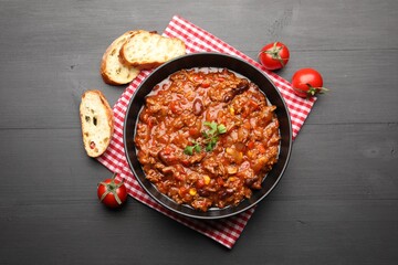 Delicious chili con carne served on black wooden table, flat lay