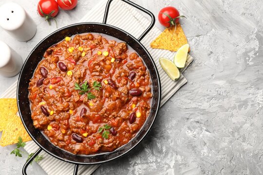 Delicious chili con carne served on textured grey table, flat lay. Space for text