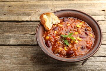 Delicious chili con carne served on wooden table, closeup. Space for text