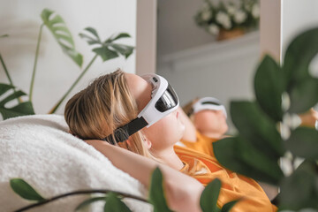 Gen Z woman unwinds  home smart eye massagerЧwellness tech  recovery, mindfulness and stress relief. Cozy greenery and soft light set a self-care, digital-detox mood, promoting balance, calm wellbeing