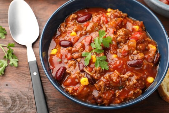 Delicious chili con carne served on wooden table, closeup