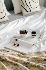 Cozy hotel bedroom with fresh cherries and coffee on a white bedspread