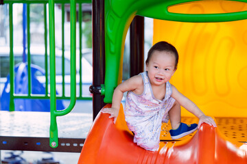 A happy toddler showing agility and joy while climbing an orange slide at a colorful outdoor playground. Ideal for content on child development, outdoor activities, and active childhood lifestyle.