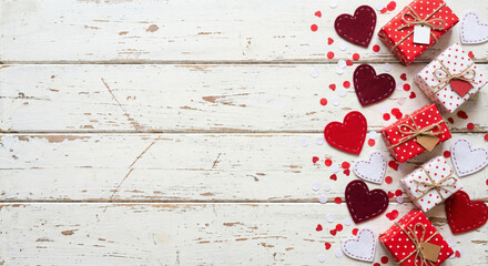 A top-down view of small red and white polka dot gift boxes arranged vertically with red and white paper hearts on a rustic white wooden background.