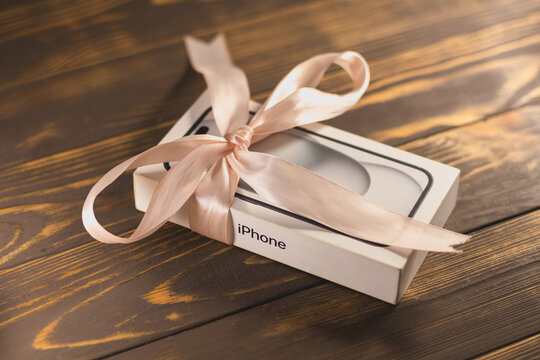 KYIV, UKRAINE - January 05, 2026 : Modern smartphone Apple iPhone in box like a present with ribbon rolled in pink bow.