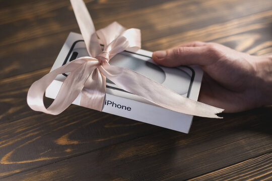 KYIV, UKRAINE - January 05, 2026 : Modern smartphone Apple iPhone in box like a present with ribbon rolled in pink bow in mans hand. Give a gift.