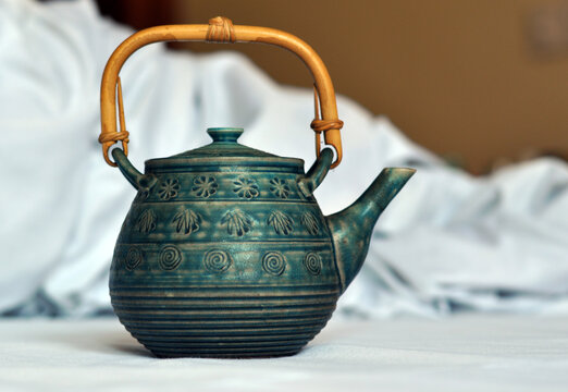Vintage turquoise patterned ceramic teapot with bamboo handle on white background. Elegant design evokes tea ceremony, cozy atmosphere, wellness and relaxation. Kitchen, cafe, spa, mindfulness 