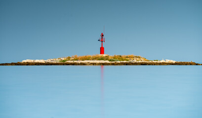 Porec, Croatia - August 13, 2025: Lonely red signal tower rising above a tiny rocky islet,...