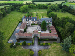 Aerial view of Chateau de la Motte Glain, a medieval castle reflecting in its surrounding moat amidst lush green fields, Oree-d'Anjou, Pays de la Loire, France.